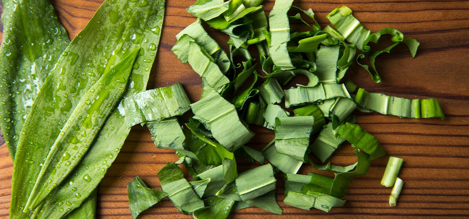 Hände, die frisch gewaschenen, leuchtend grünen Bärlauch auf einem Holzbrett sortieren.
