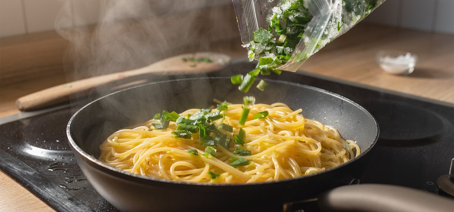 Gehackter, gefrorener Bärlauch wird aus einem Beutel direkt in eine Pfanne mit Pasta gestreut
