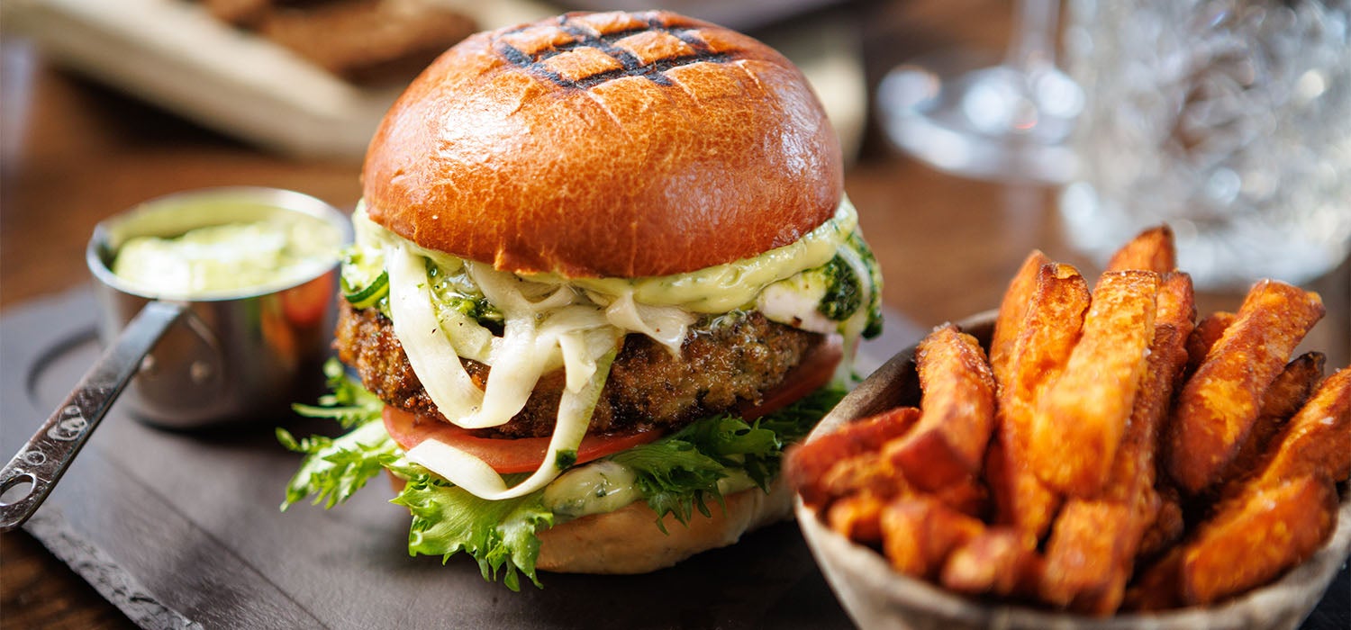 Ein Burger mit Süßkartoffel-Pommes und einem Dip, angerichtet auf einer dunklen Platte