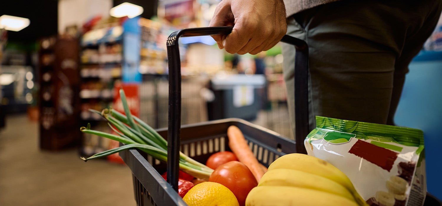 Eine Person hält einen Einkaufskorb voller frischer Lebensmittel in einem Supermarkt
