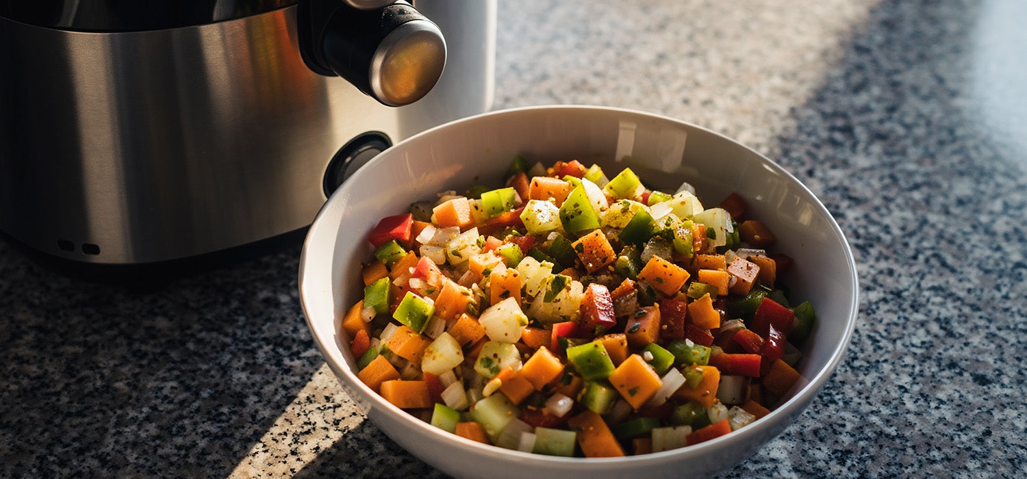 Eine Schüssel mit gewürfeltem Gemüse, das mit Öl und Gewürzen vermengt wird, daneben ein Airfryer
