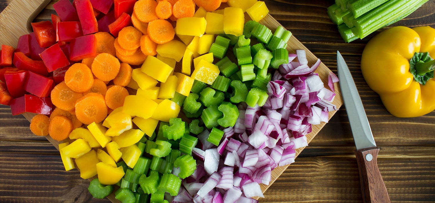 Eine bunte Auswahl an rohem, geschnittenem Gemüse (Brokkoli, Paprika, Karotten, Zucchini) auf einem Holzbrett.]