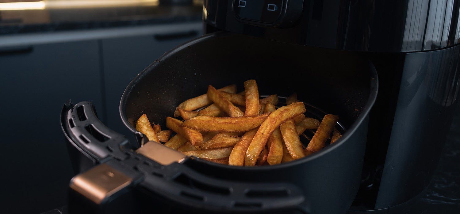 Der herausgezogene Garkorb eines Airfryers, locker gefüllt mit fertigen, goldbraunen Pommes