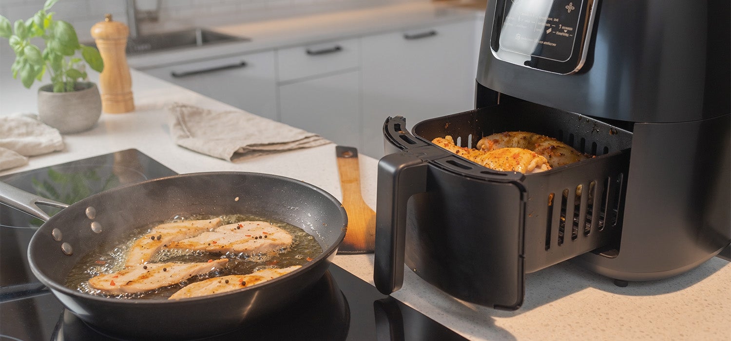 Hähnchengeschnetzeltes, das in einer Pfanne brutzelt, daneben ein Airfryer mit Hähnchenschenkel