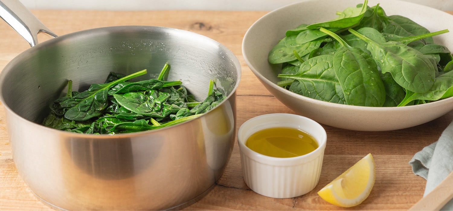 Frischer Spinat in einem Topf und daneben frischer Spinat als Salat serviert.