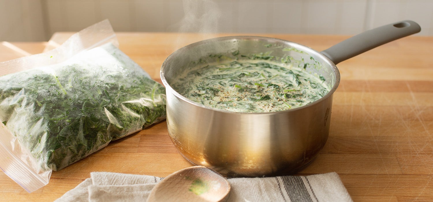 Ein Topf mit cremigem Spinat, daneben eine Packung TK-Spinat