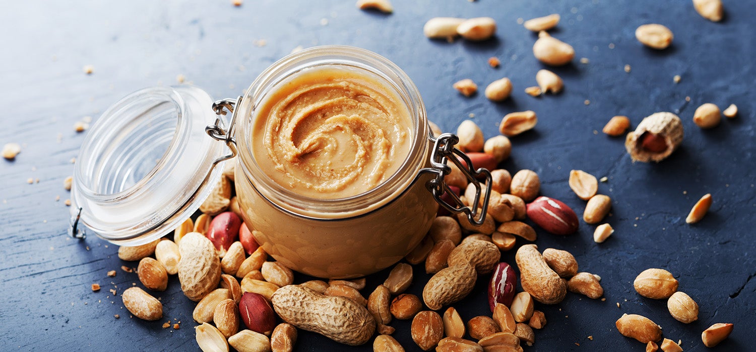 Erdnussbutter in einem Einmachglas, daneben Erdnüsse