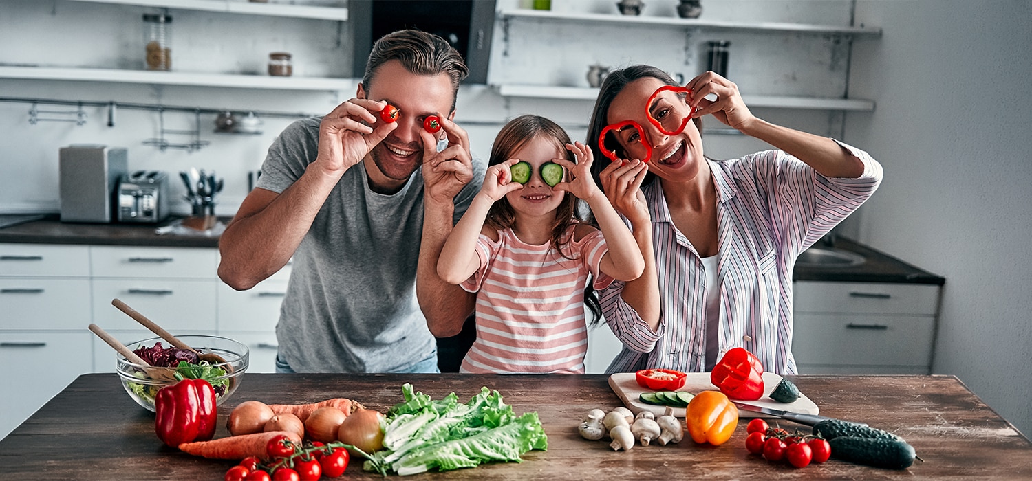 Eine Familie bestehend aus Vater, Mutter und Kind schneiden Gemüse und haben Spaß dabei.