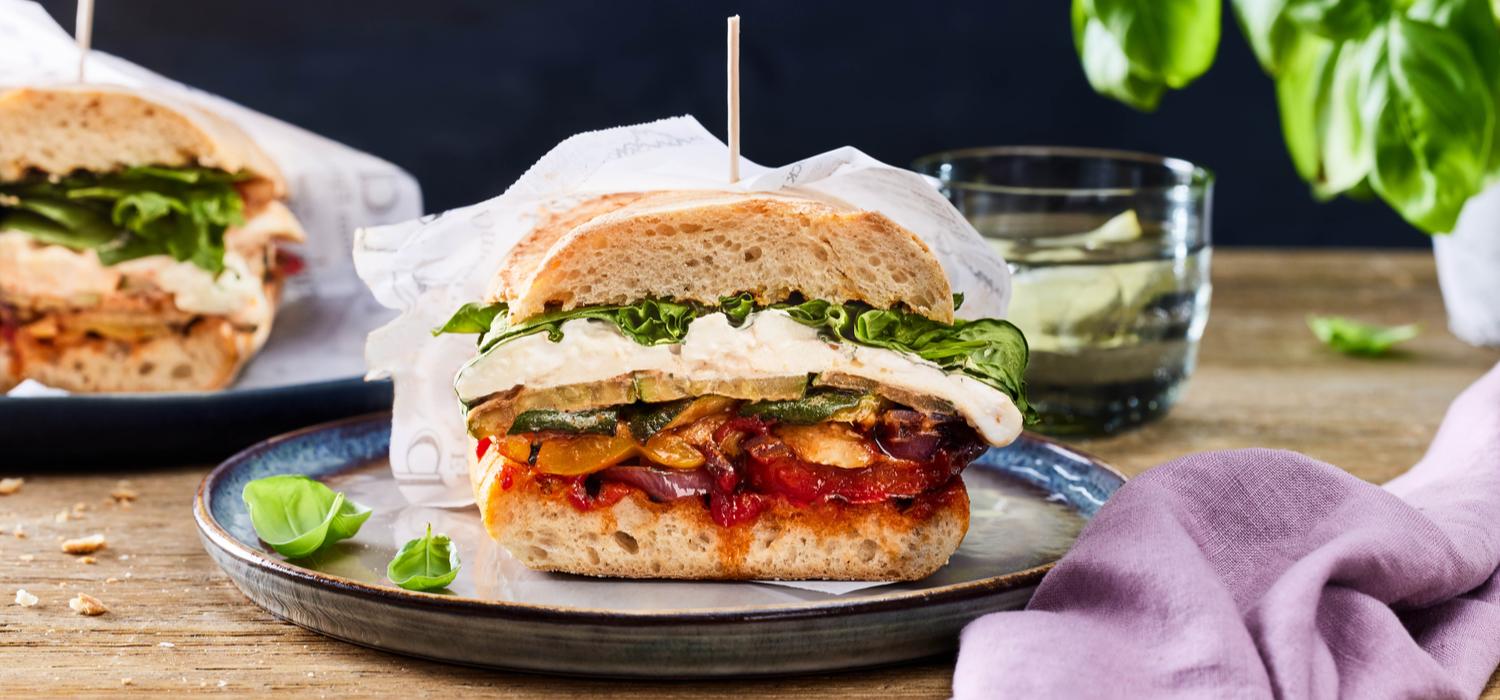 Ein in die Hälfte geschnittenes Grillgemüse Sandwich serviert auf einem Teller