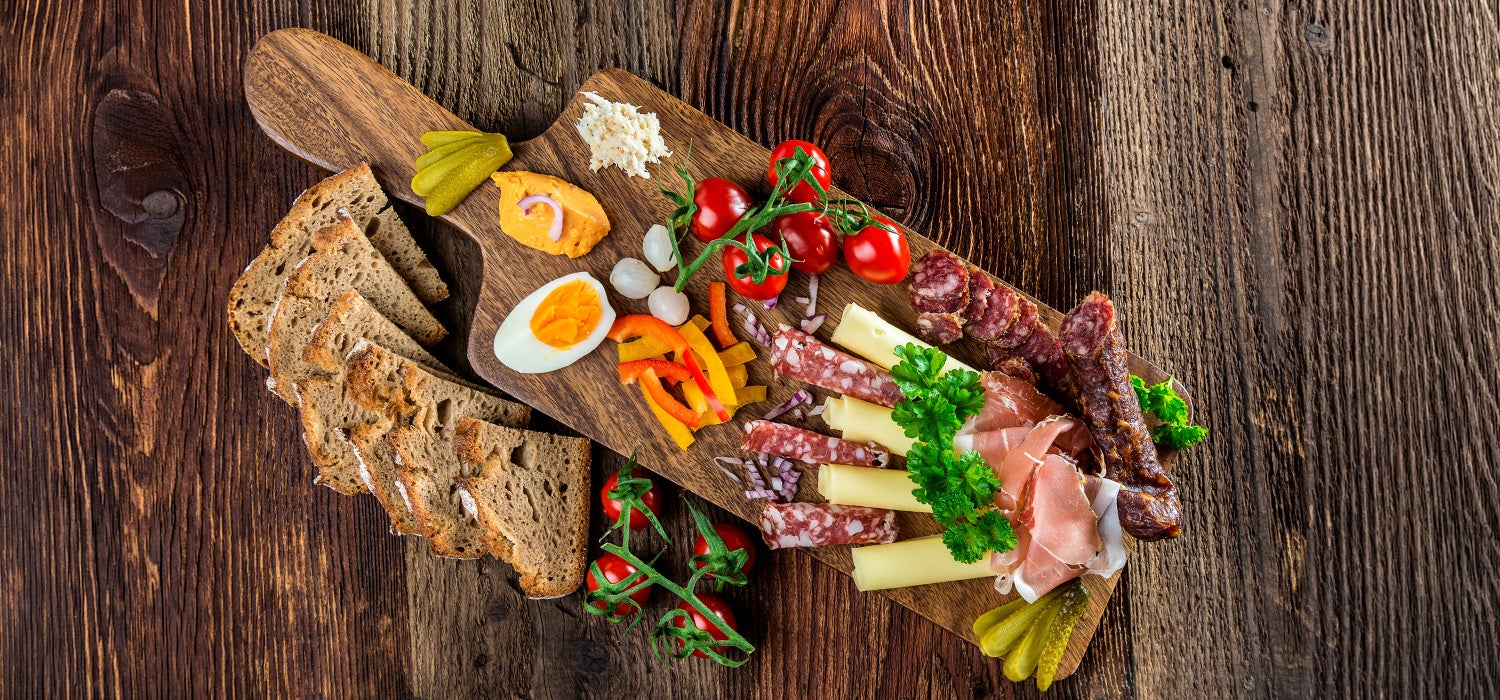 Brotzeit schön angerichtet auf einer Holzplatte mit verschiedenem Gemüse, Wurst, Käse und Brot