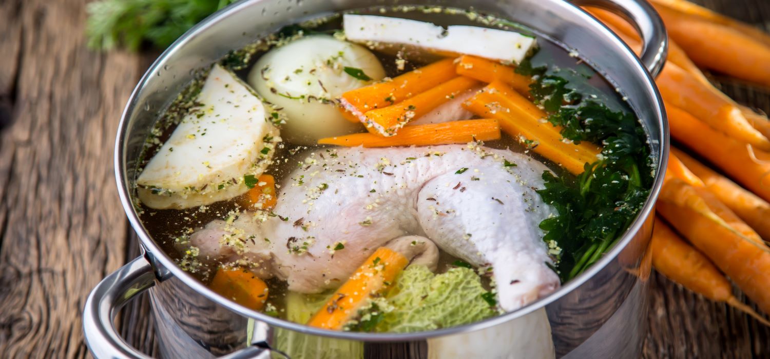 Klare Hühnerbrühe mit Kohlrabi, Möhren und weiterem Gemüse in einem Topf.