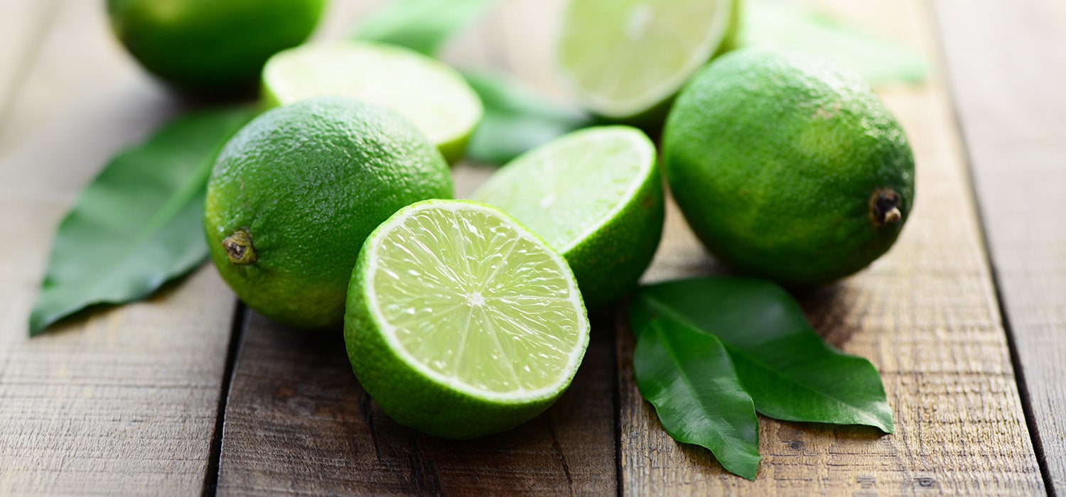 Viele Limetten auf einem Holzbrett, einige davon sind in 2 Hälften geschnitten.