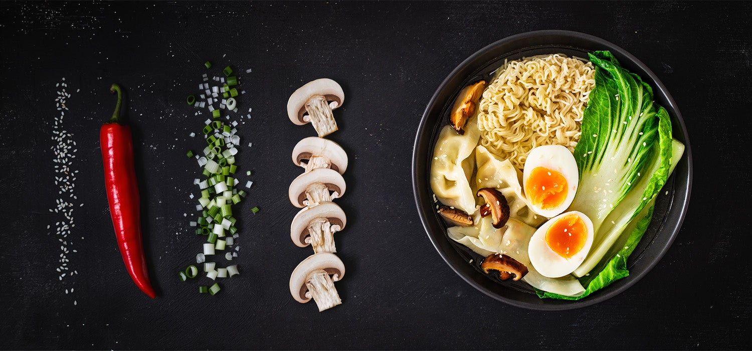 Vegetarische Toppings für Ramen: Champignons, Frühlingszwiebeln, Chili, Sesamsamen neben einer Schüssel mit Ramen.