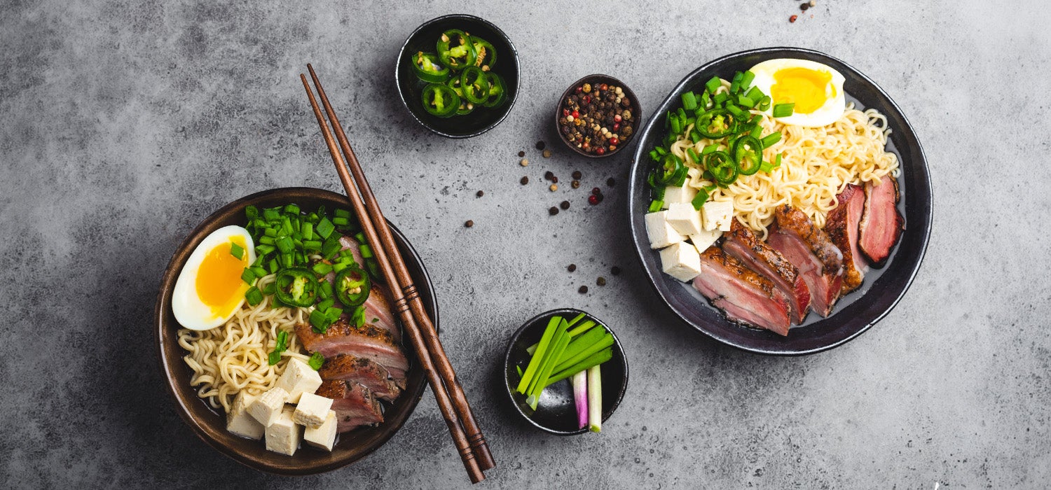 zwei Ramenschüsseln mit Ramen, getoppt mit Ei, Frühlingszwiebeln, Chili, Ente und Tofu.