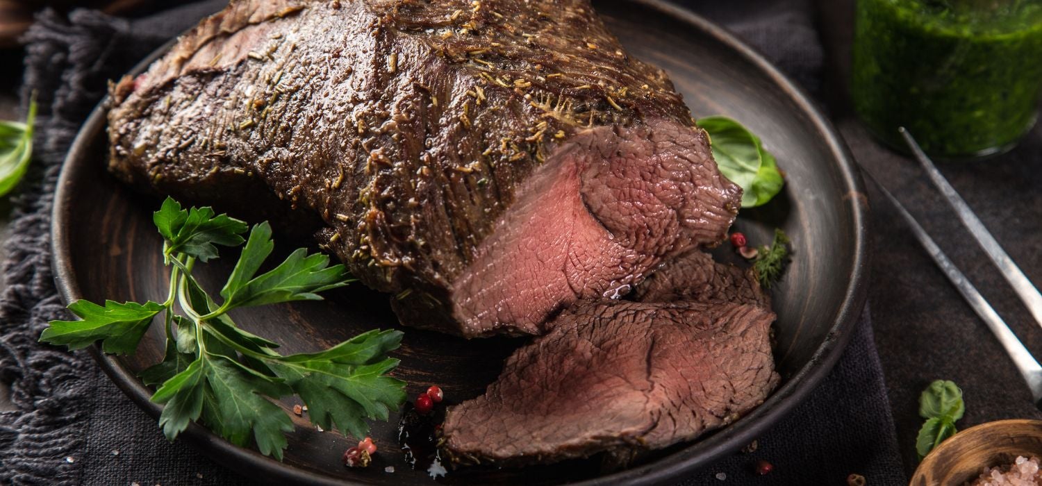 Rinderbraten garniert mit Kräutern und Gewürzen serviert auf einem Teller in Holzoptik.
