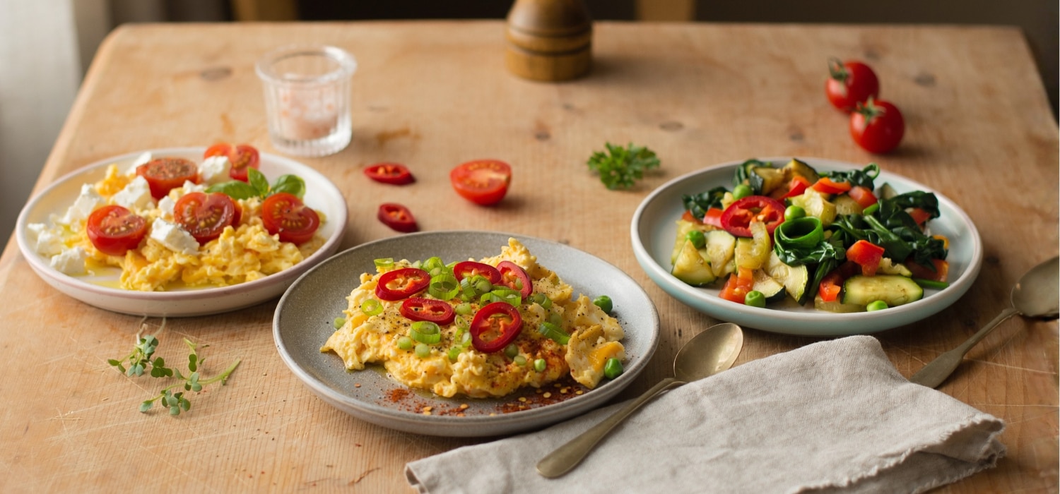 Drei kleine Teller mit verschiedenen Rührei-Variationen: eine mit Tomate/Feta, eine mit Chili/Maggi Würze Hot und eine mit Gemüse