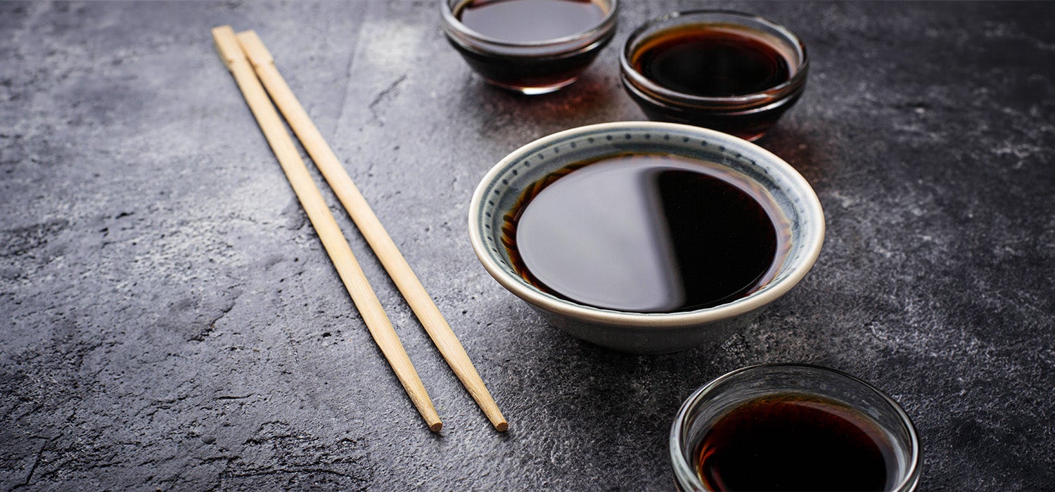 Sojasauce in einer Schüssel, daneben Sushistäbchen. 