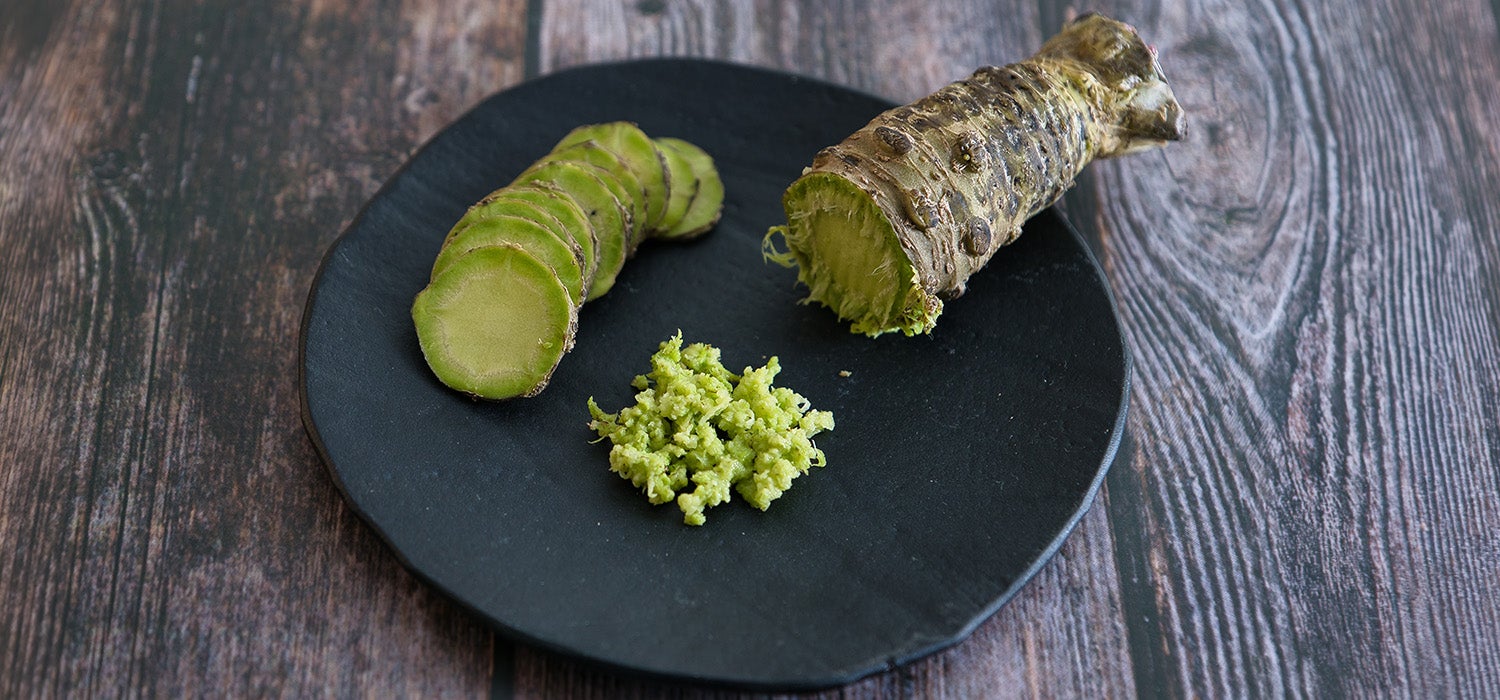Wasabi als ganzer Wurzelstock, in Scheiben geschnitten und als Paste auf einem Teller platziert.