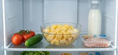 Glasschüssel mit Eierwürfeln im Kühlschrank, daneben Tomaten, Gurke, Milchflasche und verpacktes Fleisch.