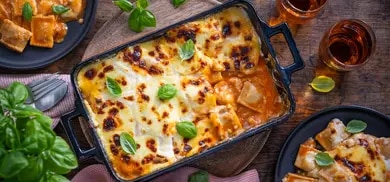 Ravioli-Lasagne in Auflaufform mit geschmolzenem Kaese, Tomatensauce und Basilikum auf Holztisch