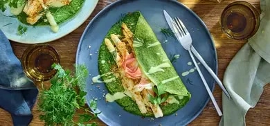 Gefüllter Kräuterpfannkuchen mit paniertem Spargel, heller Sauce, Schinken und Kräutern auf Teller