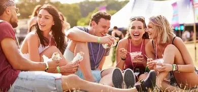 Gruppe sitzt auf Wiese bei Festival und isst Snacks aus Bechern und Wraps