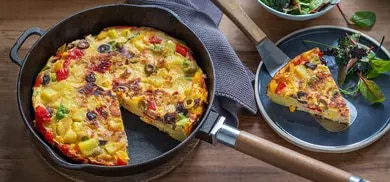 Frittata mit Raclettekaese in Pfanne, Gemuesestuecke, angeschnittene Scheibe auf Teller