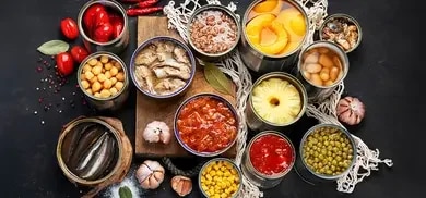 Geoeffnete konservendosen mit bohnen, mais, tomaten, ananas und fisch auf dunkler oberflaeche