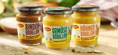 Drei Maggi Bouillon-Glaeser mit Rinder-, Gemuese- und Huehnerbouillon auf Holzoberflaeche