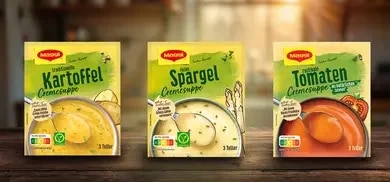 Drei Maggi Cremesuppen Packungen mit Kartoffel-, Spargel- und Tomatensuppe auf Holztisch vor Kueche