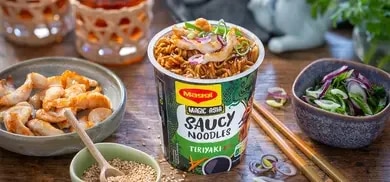MAGGI Saucy Noodles Teriyaki Cup mit Haehnchenstreifen und Fruehlingszwiebeln auf Tisch mit Zutaten