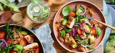 Nudelsalat mit gegrilltem Haehnchen, Avocado, Tomaten und roten Zwiebeln auf zwei Tellern