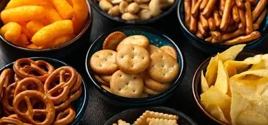 Schalen mit Salzbrezeln, Crackern, Chips, Erdnüssen und Mais-Snacks auf dunkler Oberfläche