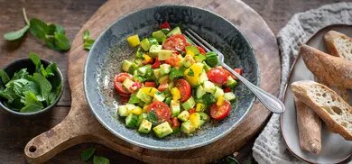 Schale mit Avocadosalat aus gewuerfelter Avocado, Gurke, Tomaten und Paprika, daneben Baguettescheiben