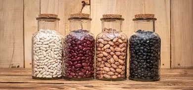 Vier Glasbehälter mit weißen, roten, gesprenkelten und schwarzen Bohnen auf Holztisch.