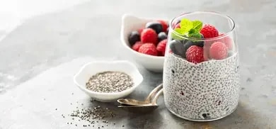 Chia-Pudding im Glas mit Himbeeren, Blaubeeren und Minzblättern auf grauer Oberfläche
