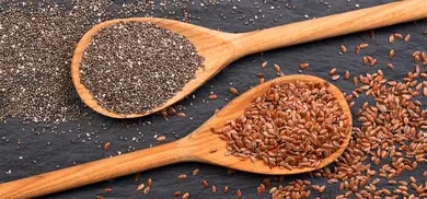 Chiasamen und Leinsamen auf Holzlöffeln mit verstreuten Samen auf dunkler Steinoberfläche