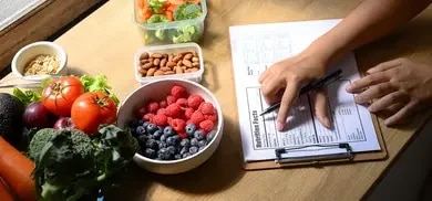 Schale mit Beeren, Gemuese, Mandeln und Ernaehrungstabelle auf Klemmbrett