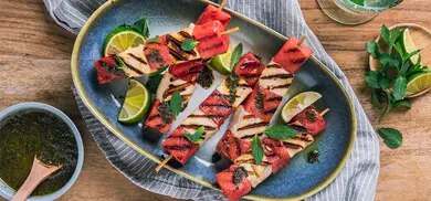 Gegrillte Spiesse mit Halloumi und Wassermelone, serviert mit Limettenspalten und Kraeutern auf Teller