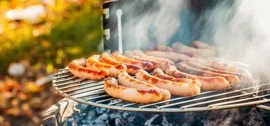 Mehrere gegrillte Würstchen auf Rost über Holzkohlegrill mit Rauchentwicklung