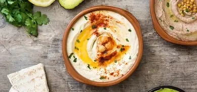 Schalen mit Hummus und Bohnencreme, Avocado, Zitrone, Petersilie und Pitabrot auf Holztisch
