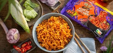 Schale mit Instantnudeln, daneben Maggi Korean Kimchi Chicken Packung, Knoblauch, Chili und Frühlingszwiebeln