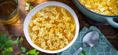 Schale mit klarer Suppe und Shrek-förmigen Nudeln, daneben Löffel und Topf