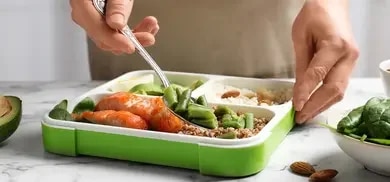 Aufgeteilte Lunchbox mit Lachs, gruenen Bohnen, Getreide, Avocado und Mandeln