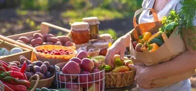Person mit Papiertüte voller Gemüse an einem Marktstand mit Obst und Gemüse