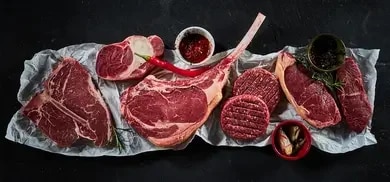Verschiedene rohe Rindfleischstücke, Steaks und Hackfleisch mit Gewürzen auf dunklem Untergrund angerichtet