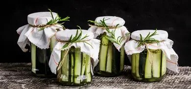 Vier Glaeser mit eingelegten Zucchinistiften und Rosmarinzweigen auf Holztisch