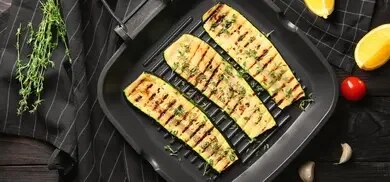 Gegrillte Zucchinistreifen in Grillpfanne mit Thymian, Zitronenspalten und Knoblauch