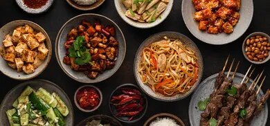 Verschiedene Gerichte mit Tofu, Nudeln, Spießen, Gurkensalat und Erdnüssen auf dunklem Hintergrund