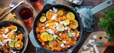Zucchini-Reis-Pfanne mit Feta in Pfanne, dazu Tellerportion und Feta auf Holzbrett